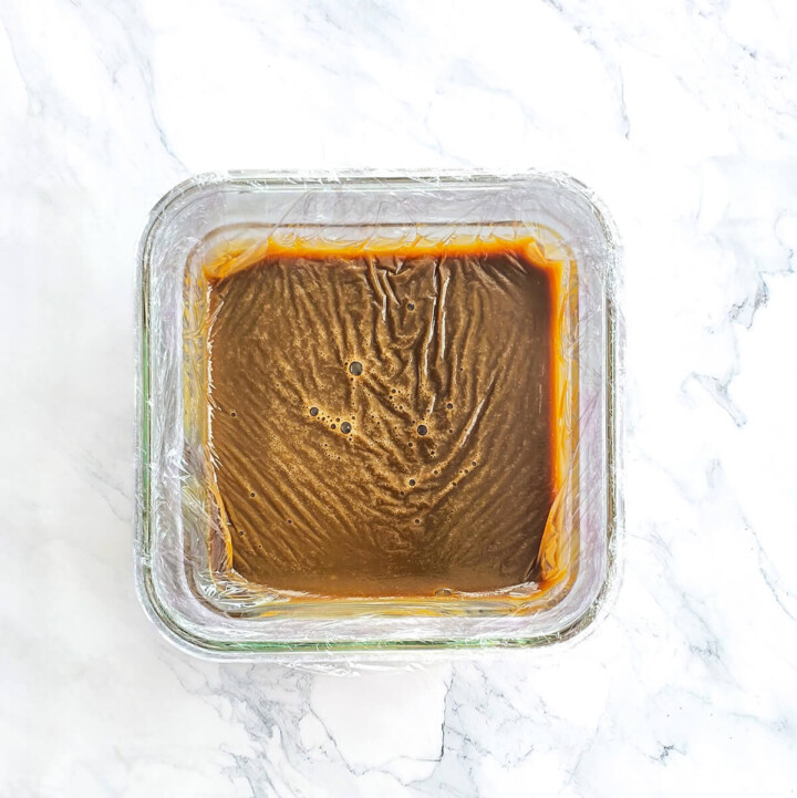 Une ganache au café filmé au contact dans un plat transparent, sur une surface blanche marbré.