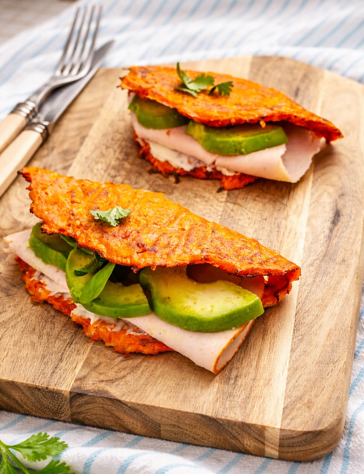 Wraps de carottes faciles et rapides, pliés en deux, garnis de tranches de blanc de dinde, d'avocat frais et d'une base crémeuse, présentés sur une planche à découper avec des couverts en arrière-plan.