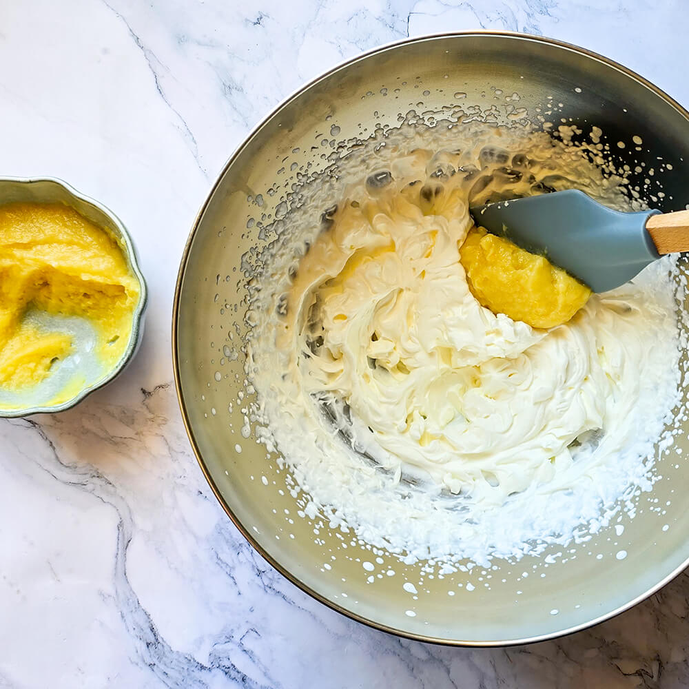 Une photo en plongée d'un bol en acier inoxydable contenant de la crème fouettée blanche et lisse avec un peu de lemon curd jaune sur le bord, et un bol plus petit sur le côté gauche avec plus de lemon curd.
