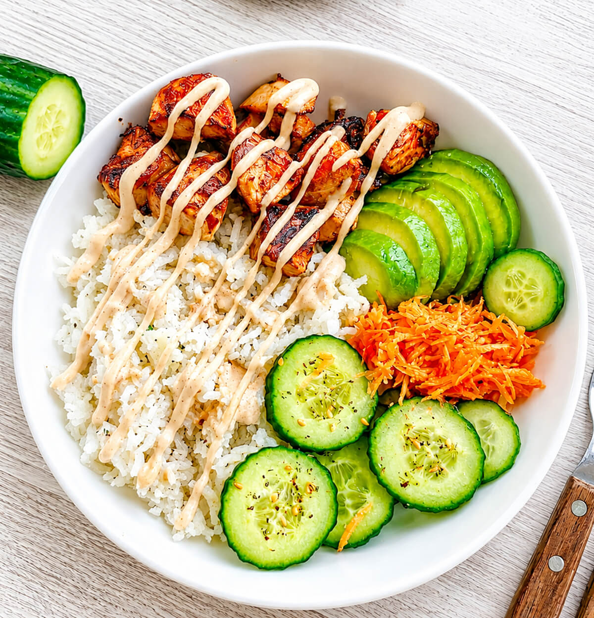 Un poké bowl composé de morceaux de saumon cuits, rondelles de concombre, tranches d'avocat et de carottes râpées, le tout nappé d'une sauce mayonnaise sriracha.