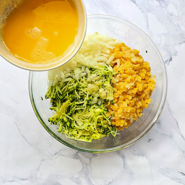 Versement d'œufs battus dans un saladier contenant des courgettes râpées, des lentilles corail cuites et des oignons émincés.