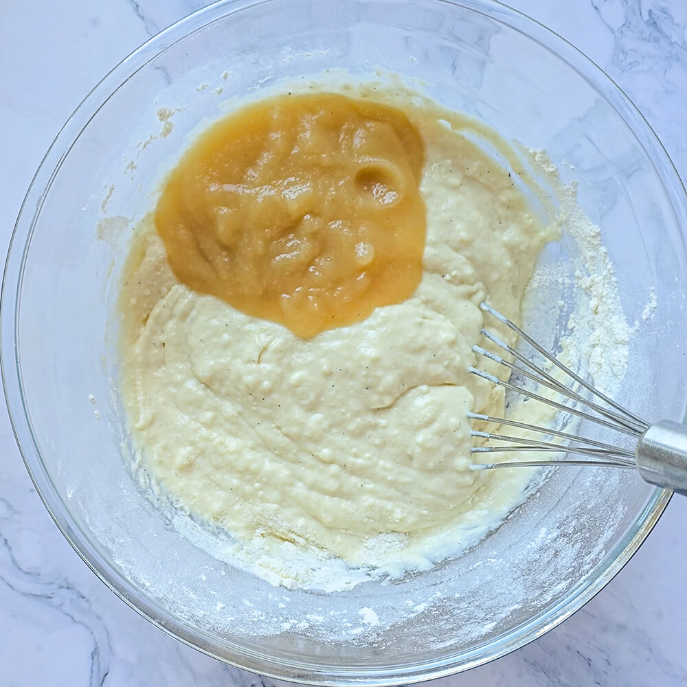 Un fouet dans un saladier en verre transparent avec une préparation pour pâte à pancakes. La compote est visible.