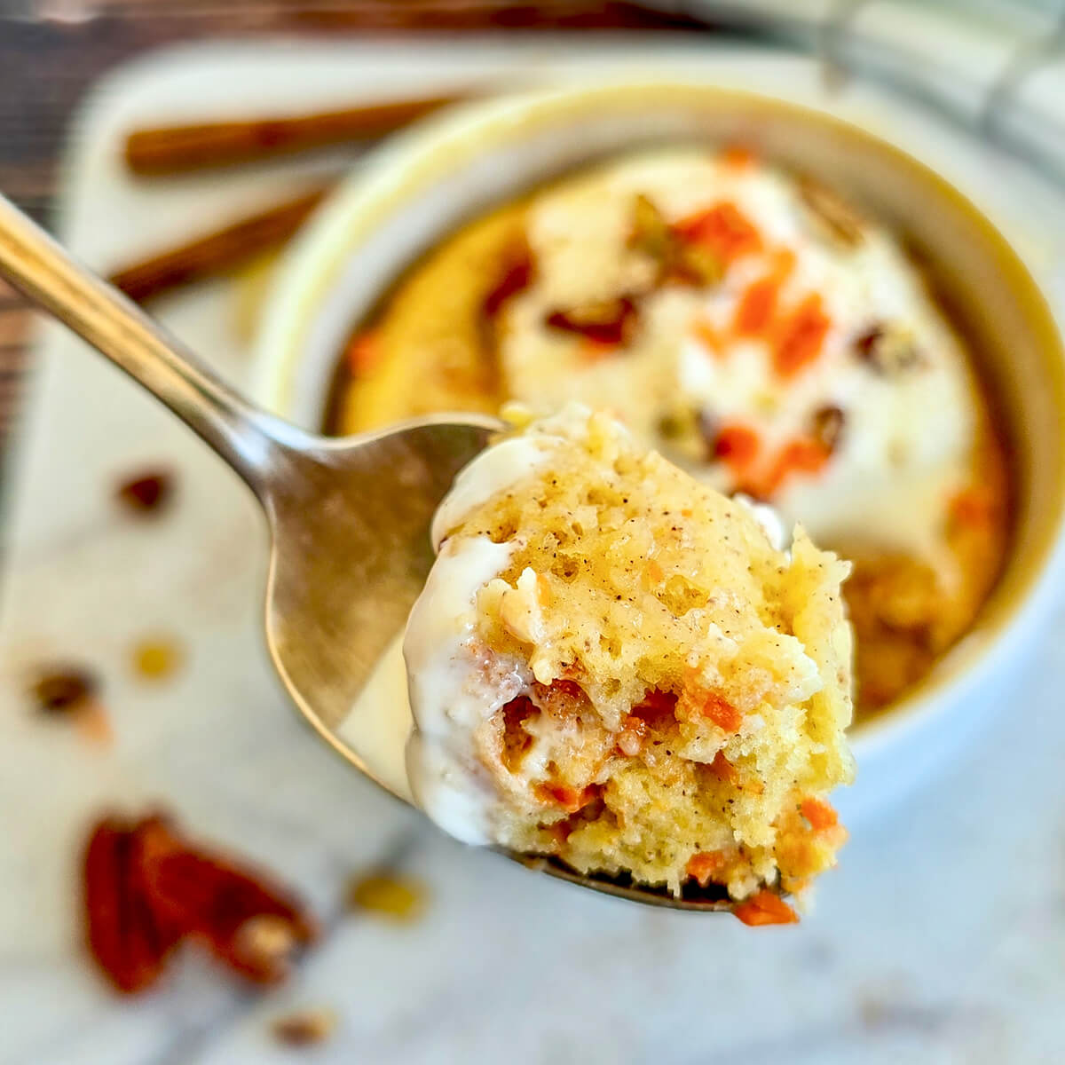 Une cuillère prélevant une bouchée moelleuse de carrot cake avec du glaçage, montrant la texture aérée de la mie, avec le bol en arrière-plan flou.