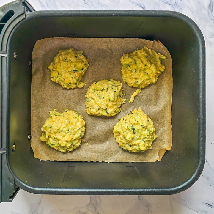 Cuisson saine de galettes de courgettes et lentilles dans le panier d'un Airfryer sur du papier sulfurisé.
