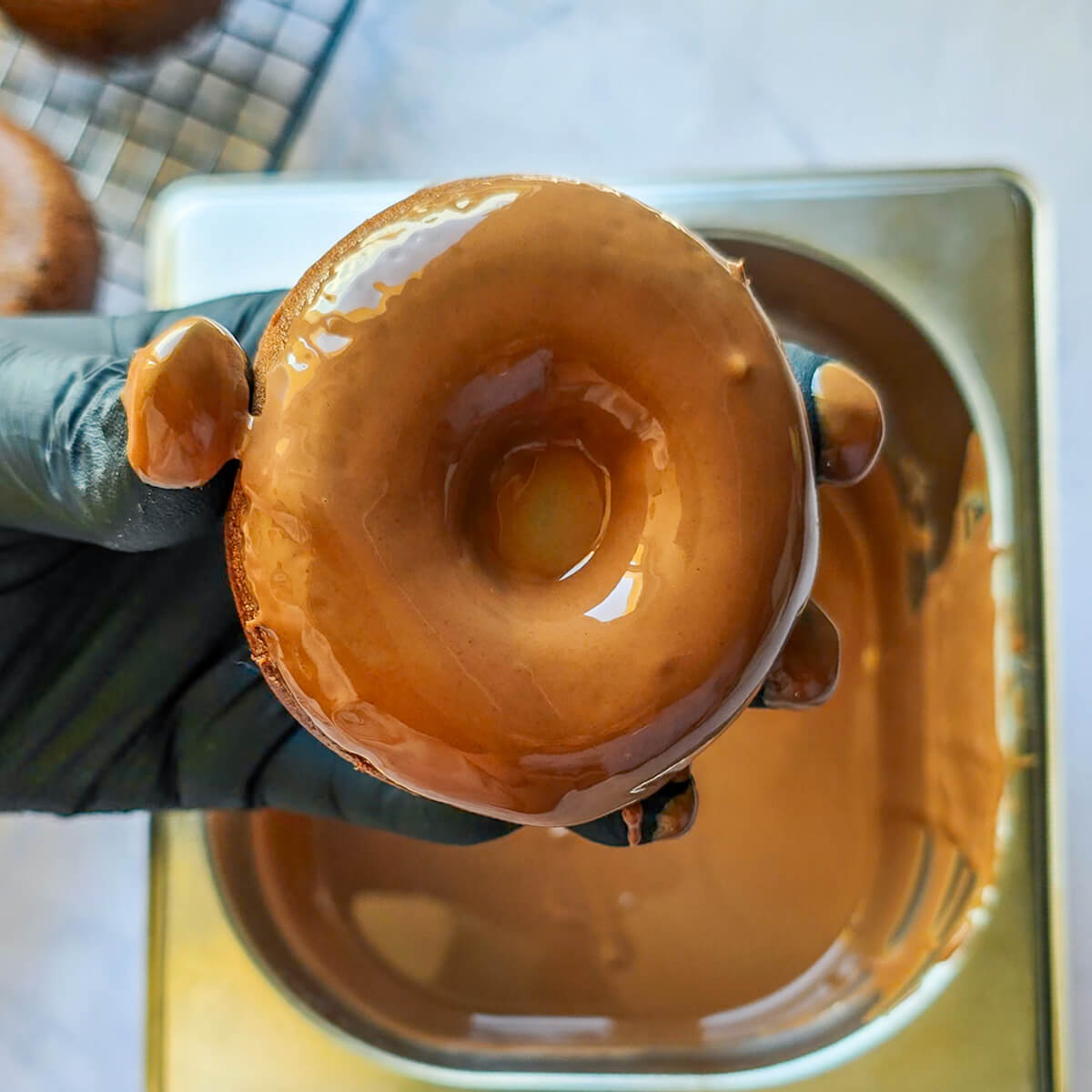 Une main trempant un donut dans du chocolat fondu pour un glaçage au chocolat au lait.