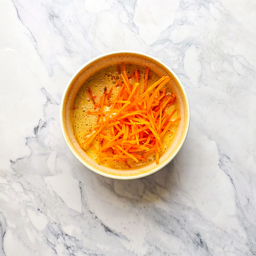 Une généreuse portion de carottes fraîchement râpées déposée sur la pâte à bowl cake avant le mélange final.