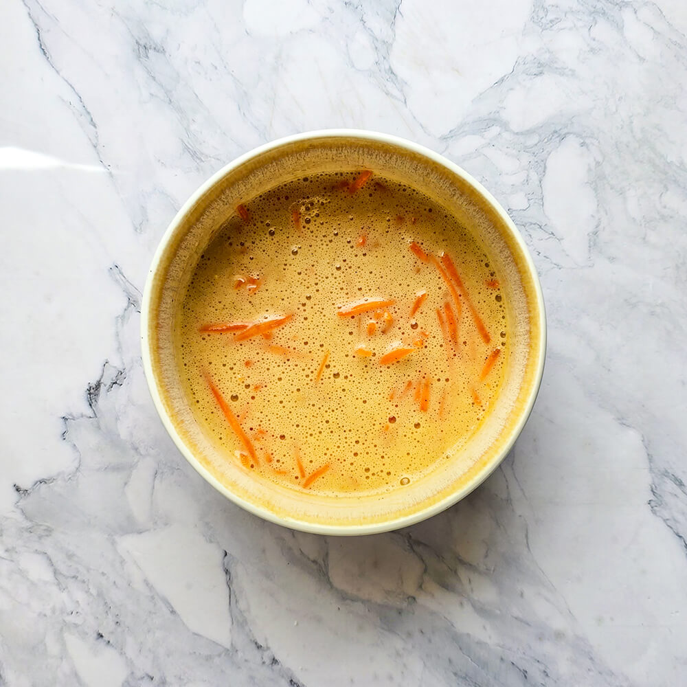La pâte homogène parsemée de morceaux de carottes, prête pour la cuisson dans son bol.