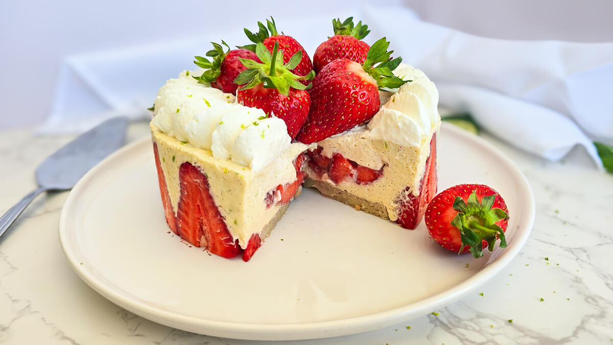 Un fraisier léger laissant apparaître une base de biscuit joconde, une crème diplomate onctueuse garnie de morceaux de fraises, et un décor de chantilly saupoudré de zestes de citron vert.