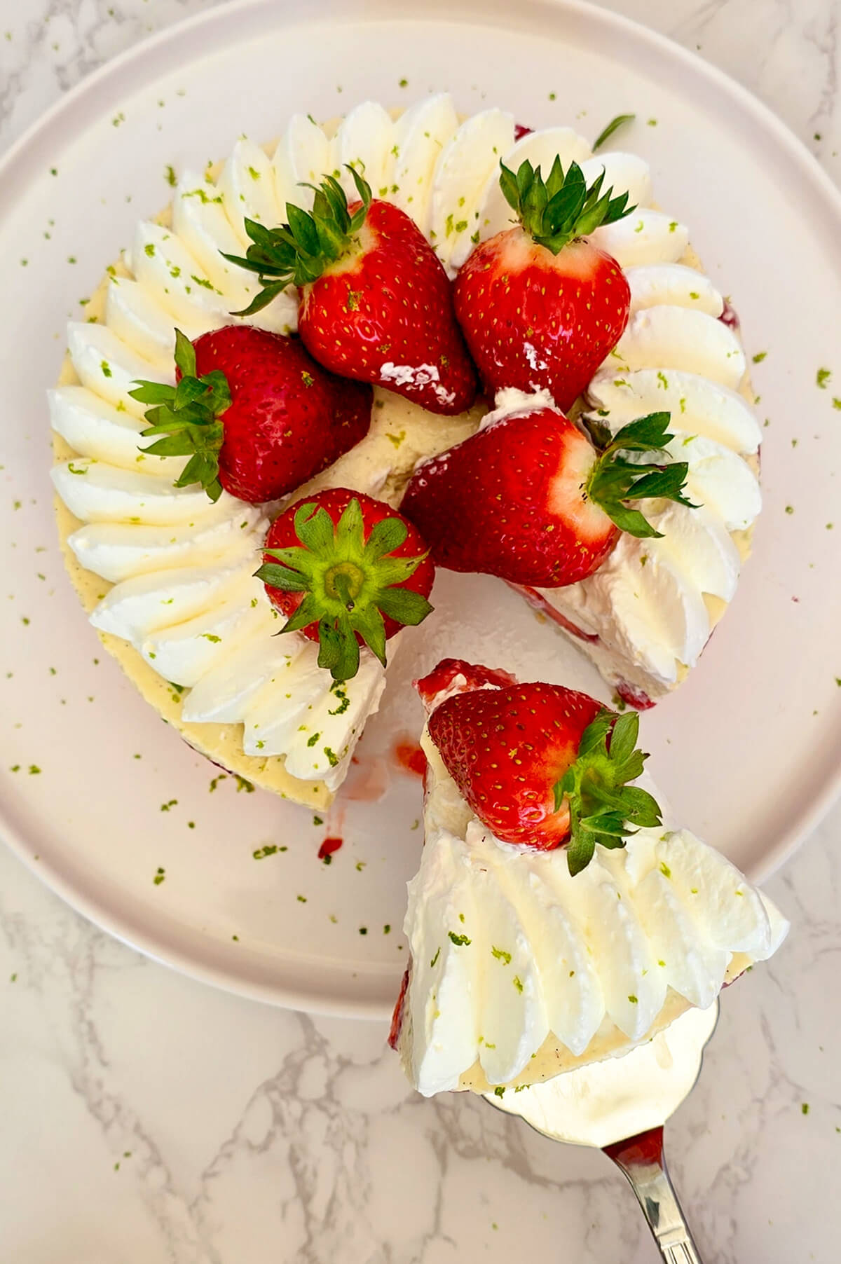 Une spatule tenant une part de fraisier léger, dans une assiette blanche.