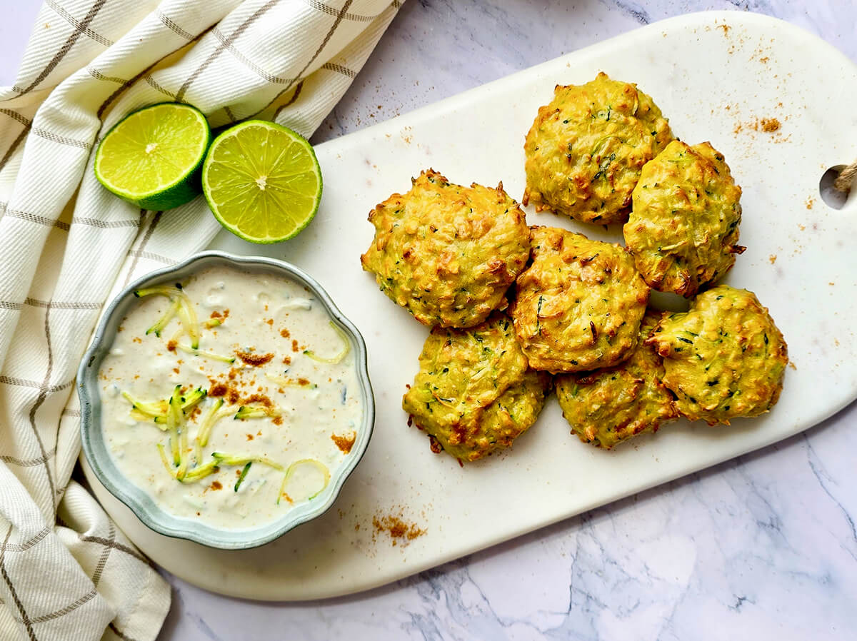 Galettes de courgettes et lentilles corail dorées à l'Airfryer, servies sur une planche blanche avec une sauce au yaourt et des quartiers de citron vert.