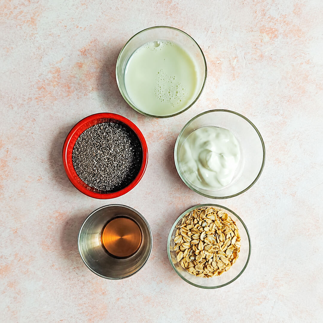 Des ingrédients de base pour une recette d'overnight oats, sur un fond rose clair.