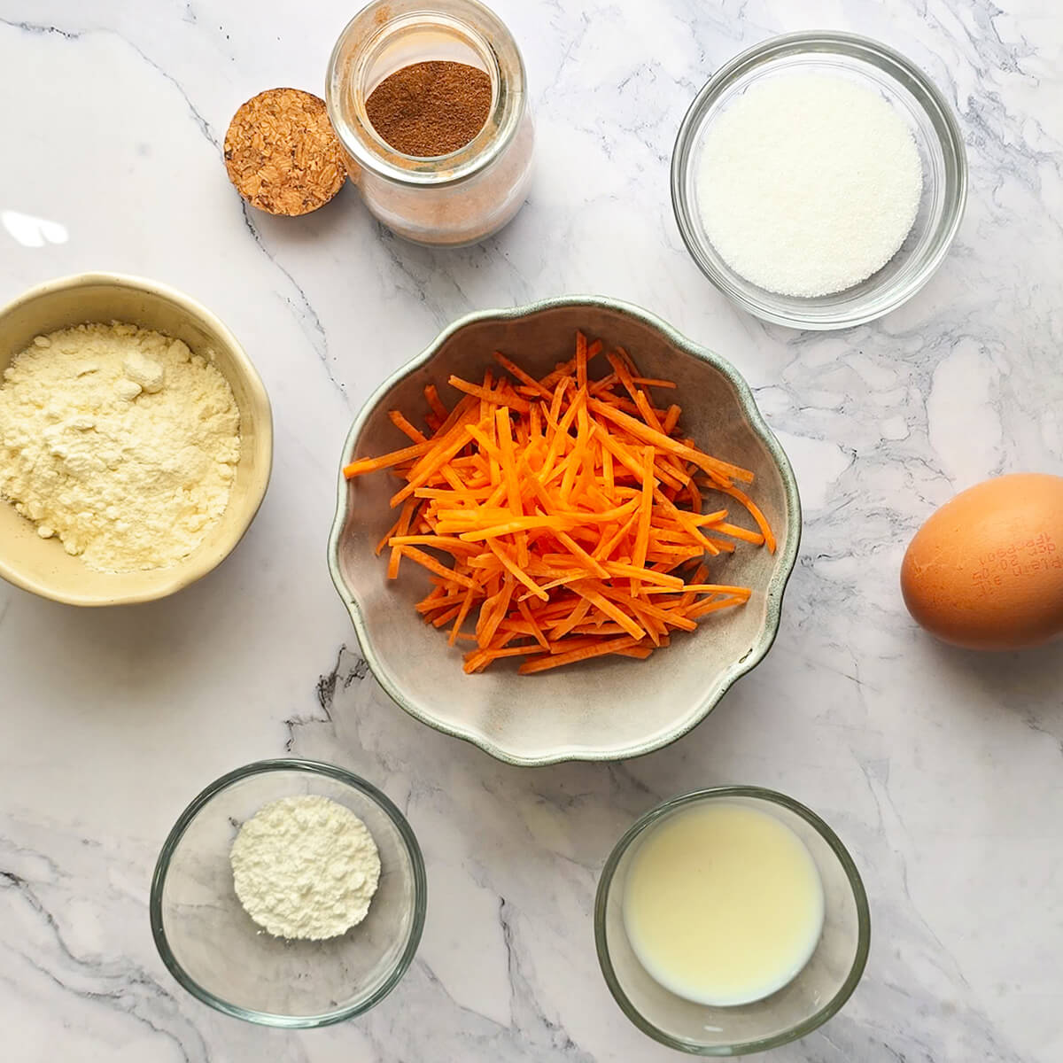 Des ingrédients pour un bowl cake façon carrot cake, sur un fond blanc marbré.