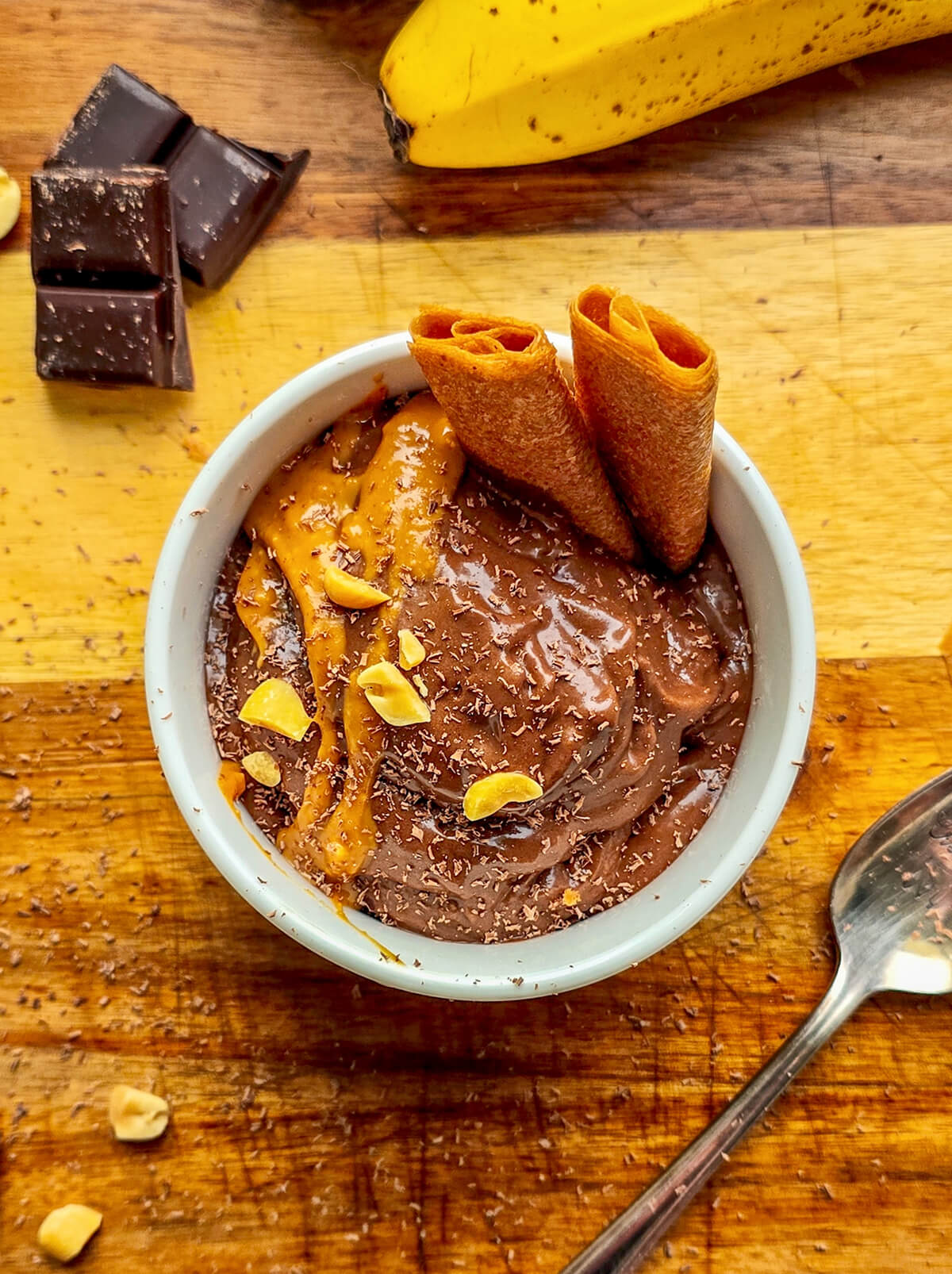Une nice cream banane chocolat avec du beurre de cacahuètes, dans un contenant en céramique blanc, sur une planche de bois.