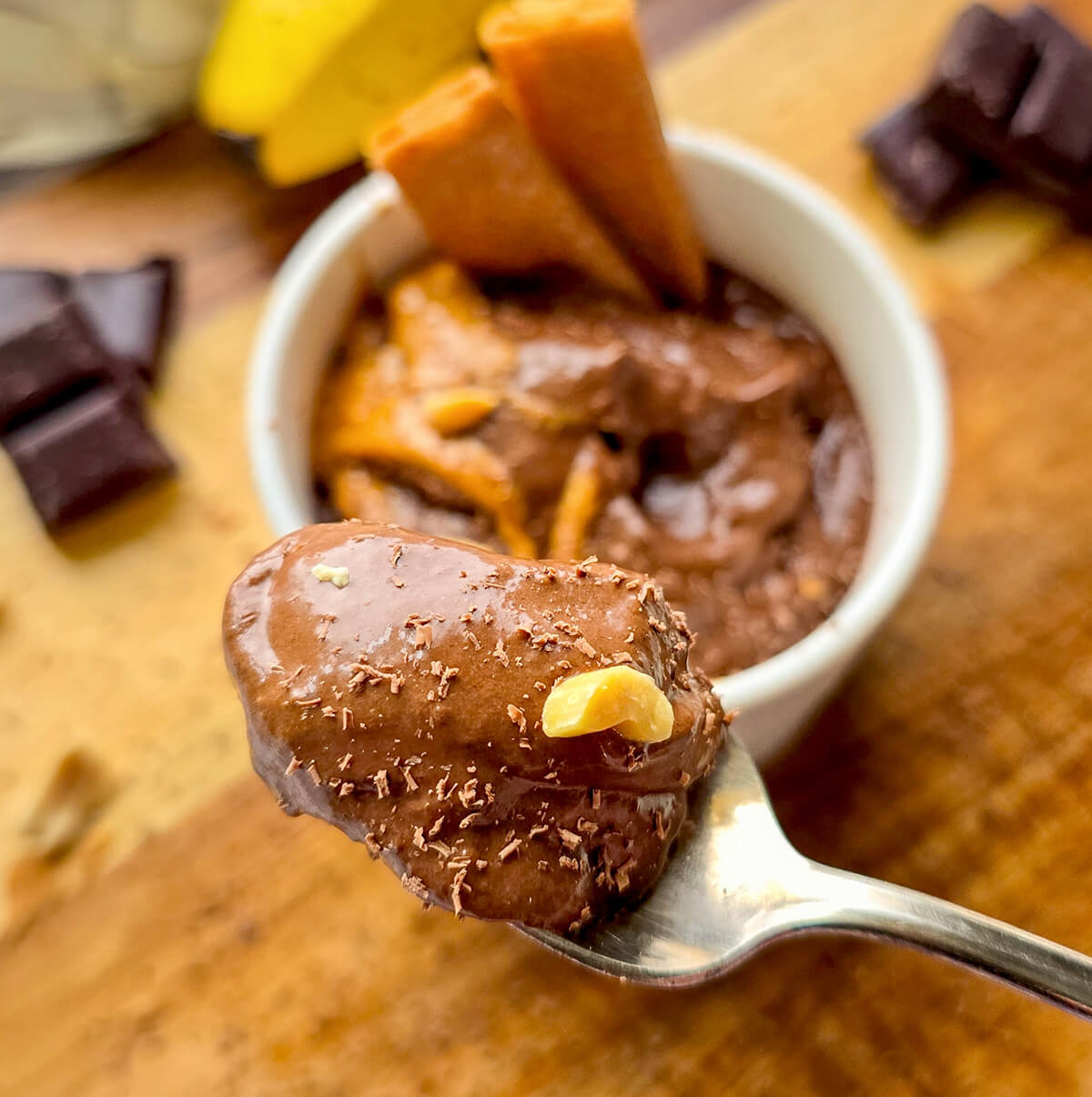 Gros plan sur une cuillère de glace banane chocolat ultra crémeuse et healthy, faite sans sorbetière. Une texture parfaite avec des éclats de cacahuètes, du beurre de cacahuètes et le bol de nice cream en arrière-plan flouté.