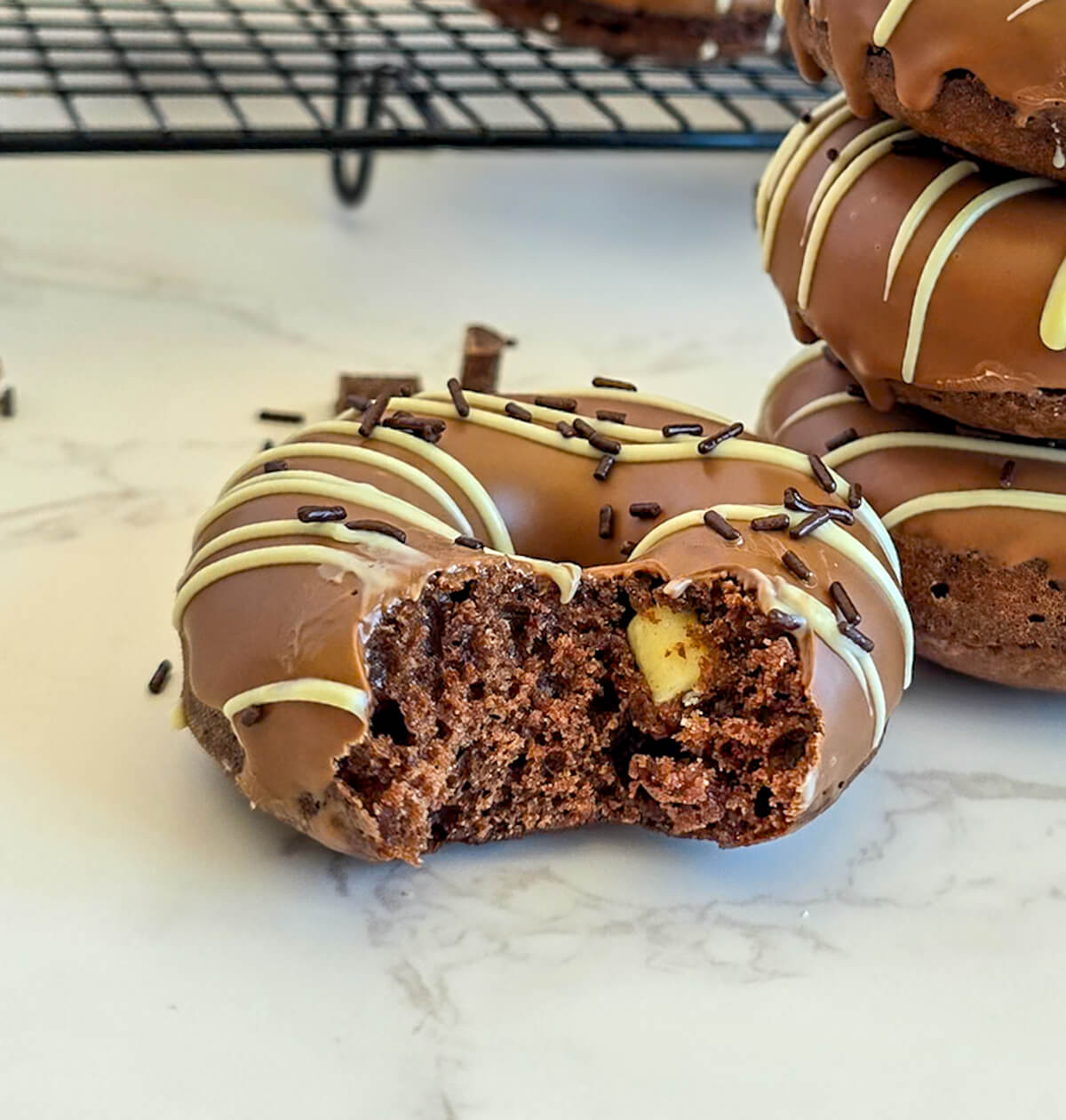 Un donut au four au chocolat ouvert, avec un morceau de chocolat blanc, posé sur une surface blanche marbrée.