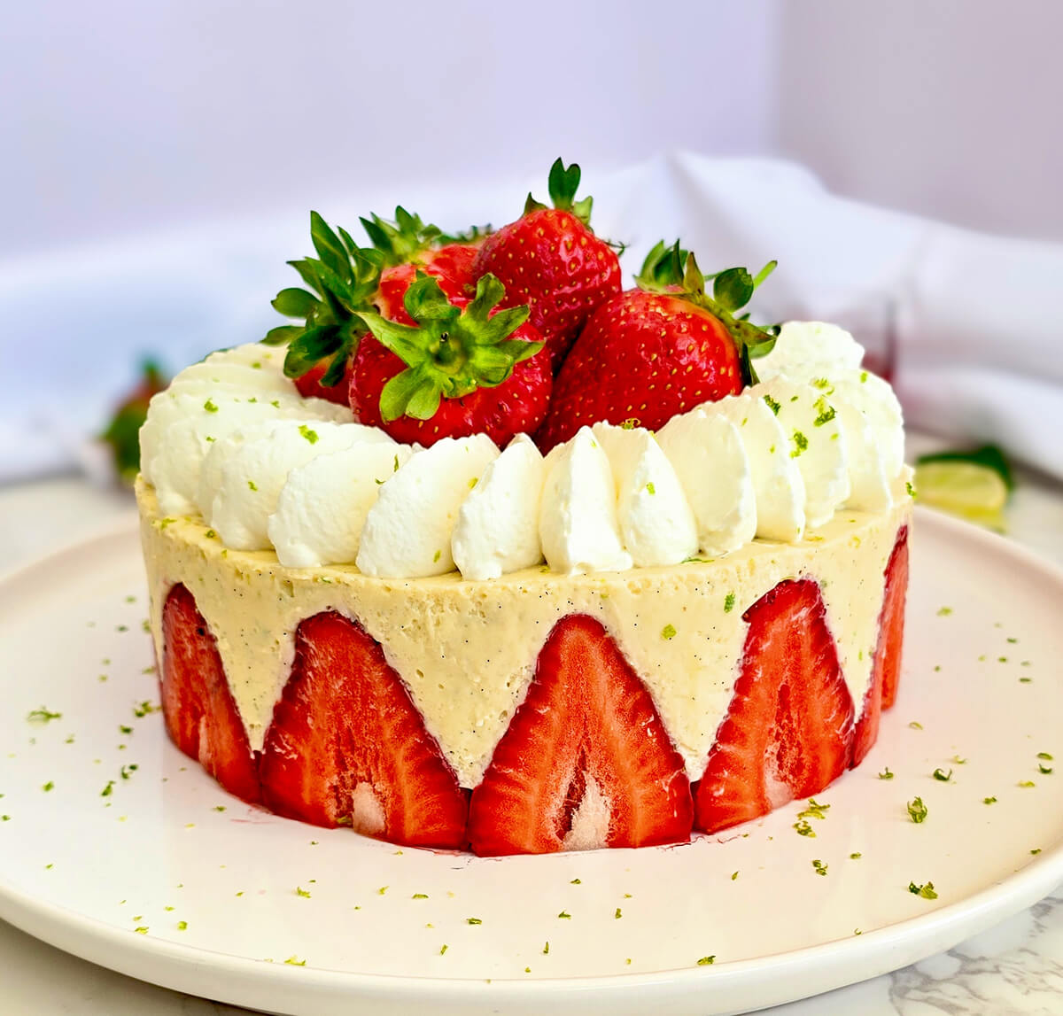Un fraisier léger et facile avec des fraises fraîches coupées en deux disposées sur tout le pourtour, garni d'une crème diplomate au citron vert, de dômes de chantilly pochés et de fraises entières sur le dessus avec quelques zestes de citron vert.