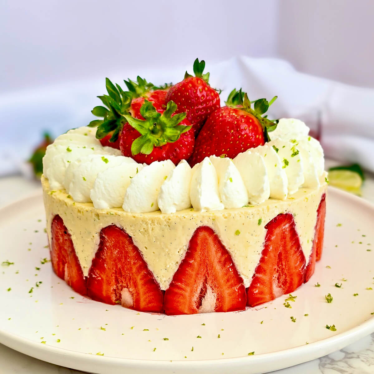 Un fraisier léger et facile avec des fraises fraîches coupées en deux disposées sur tout le pourtour, garni d'une crème diplomate au citron vert, de dômes de chantilly pochés et de fraises entières sur le dessus avec quelques zestes de citron vert.