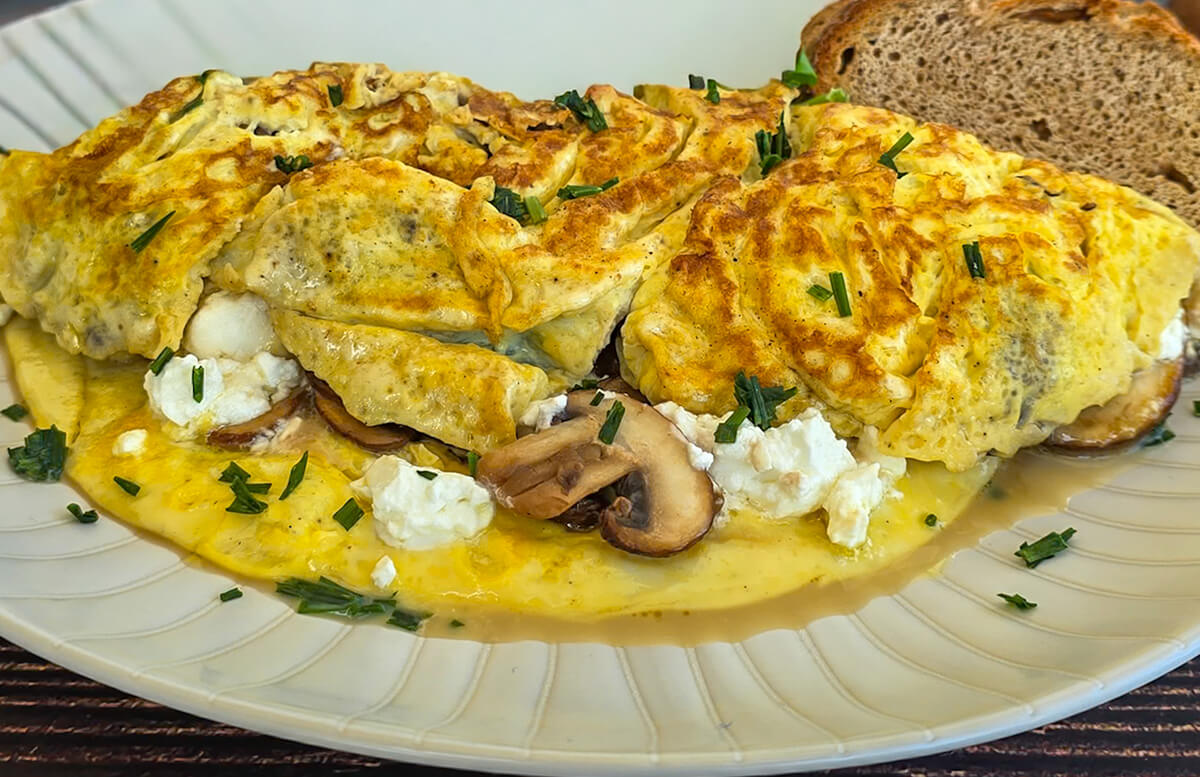 Gros plan sur une omelette moelleuse avec des champignons de Paris, de la feta et des herbes fraîches, sur une assiette blanche.