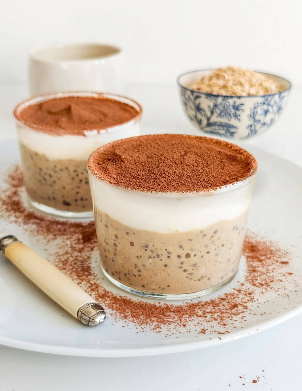 Gros plan de deux verrines de pudding d'avoine et chia au café, surmontées d'une couche de yaourt blanc et de cacao amer.