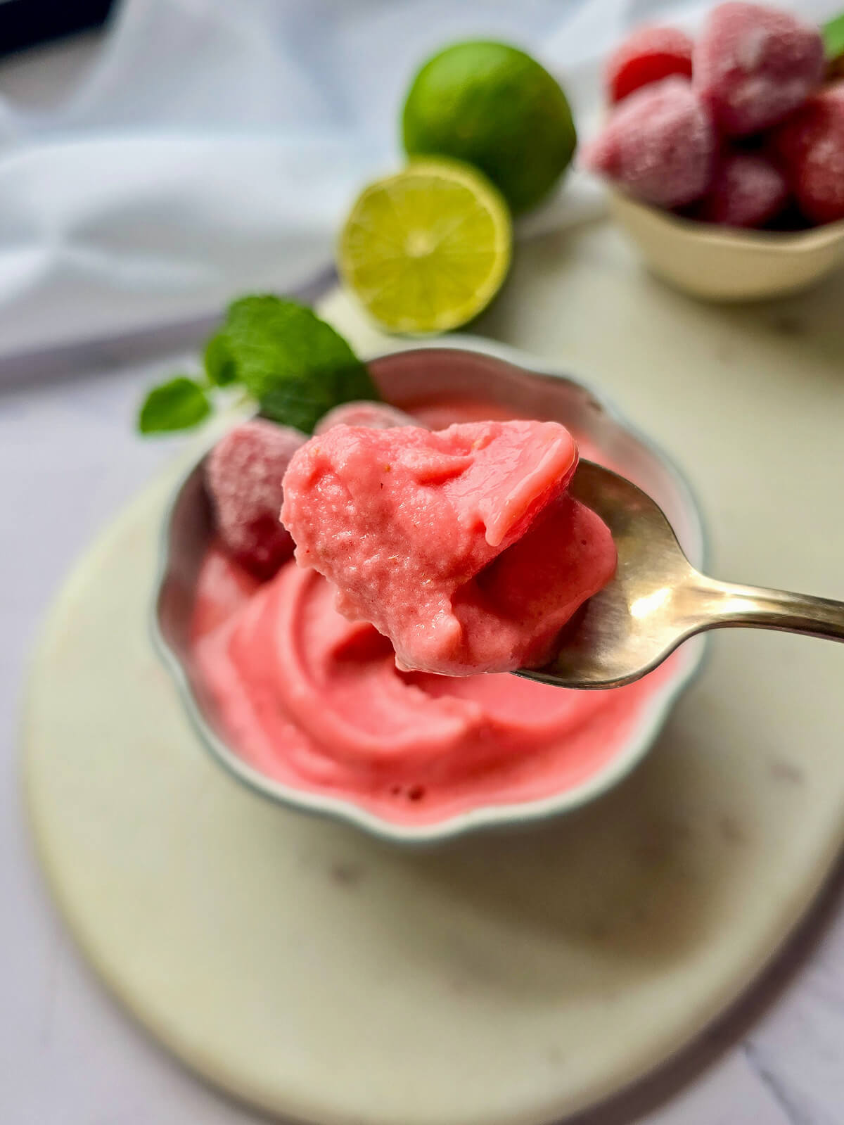 Une cuillère de sorbet fraise maison ultra crémeux, une recette facile et rapide sans sorbetière. Gros plan sur la texture parfaite de la glace à la fraise avec le bol en arrière-plan flouté.
