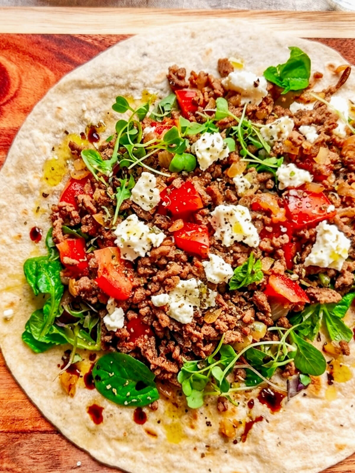 Un wrap de boeuf haché, feta, tomates, sur une planche de bois.