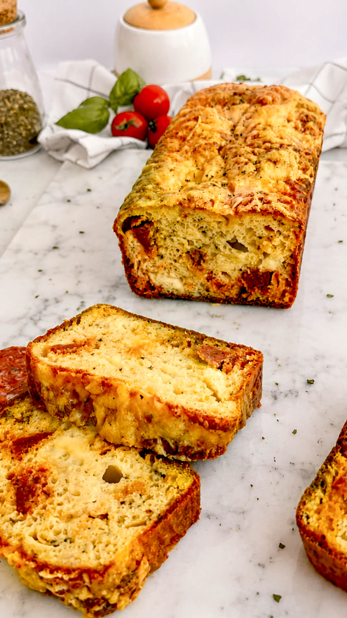 Un cake au chorizo coupé en tranches, sur une planche marbrée blanche, rondelles de chorizo et tomates cerises sur les côtés.