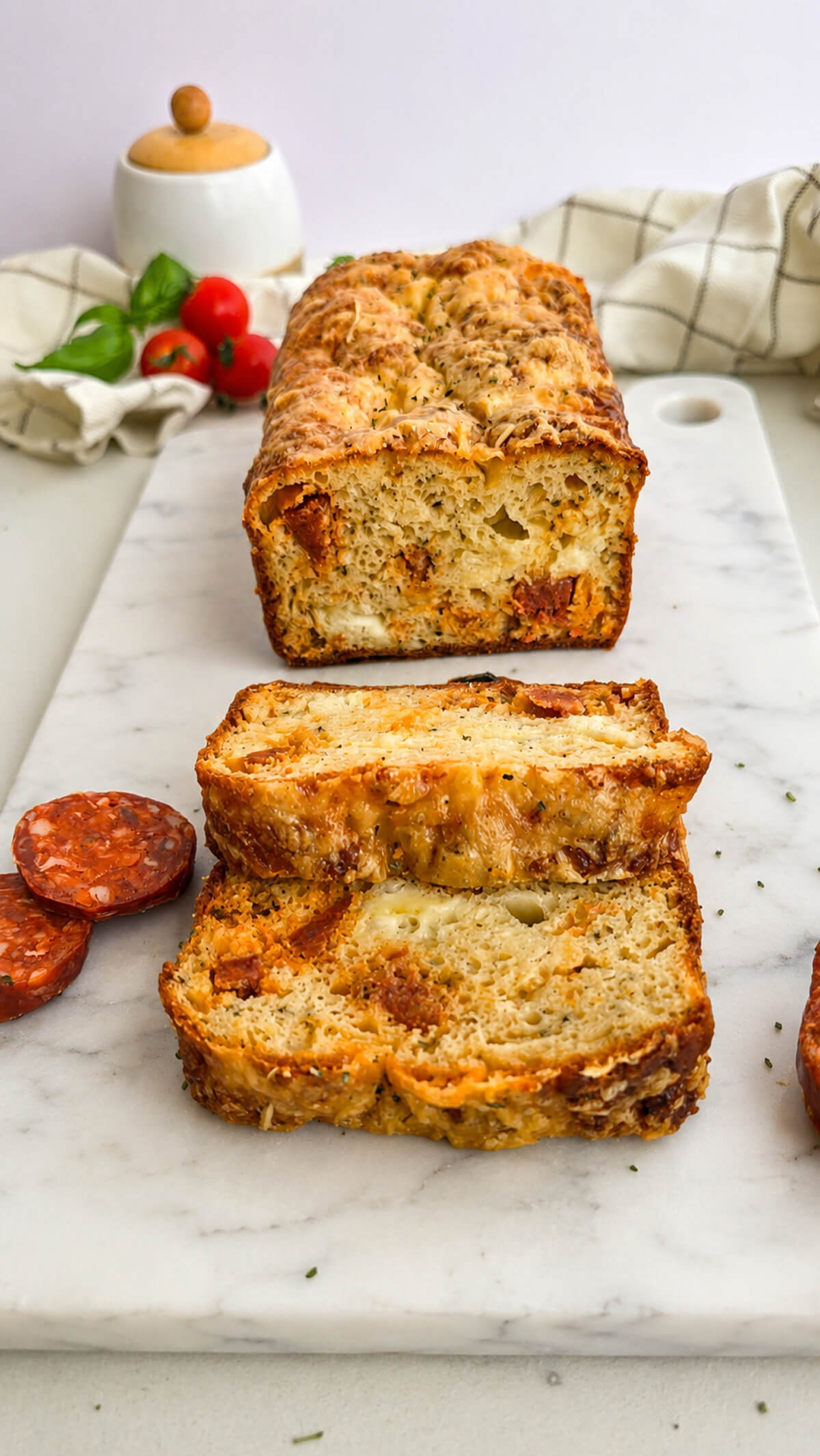 Un cake salé au chorizo coupé en tranches, sur une planche marbrée blanche, rondelles de chorizo et tomates cerises sur les côtés.