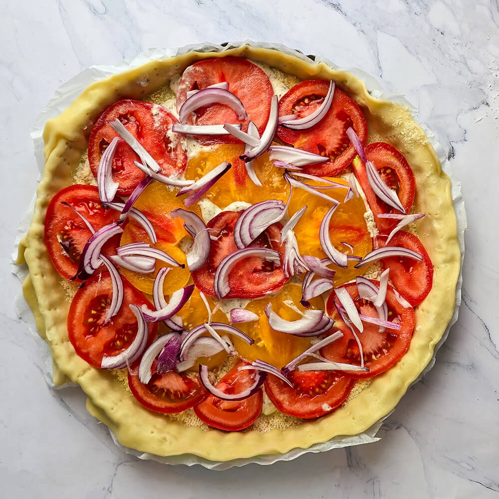 Une tarte à la tomate avant cuisson, dans son moule et sur une surface blanche marbrée