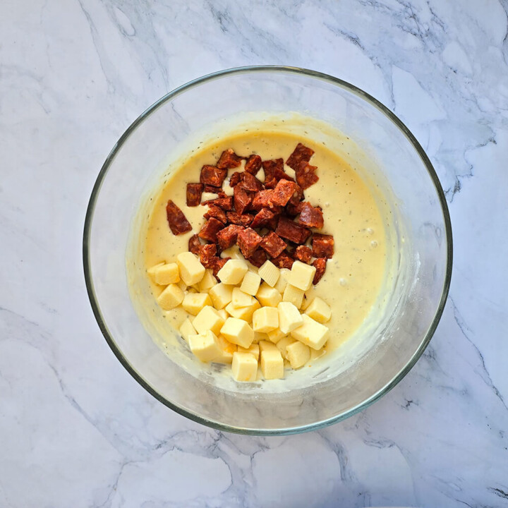 Un saladier rempli d'ingrédients tels que du chorizo et des dés de comté pour réaliser une recette de cake salé au chorizo.