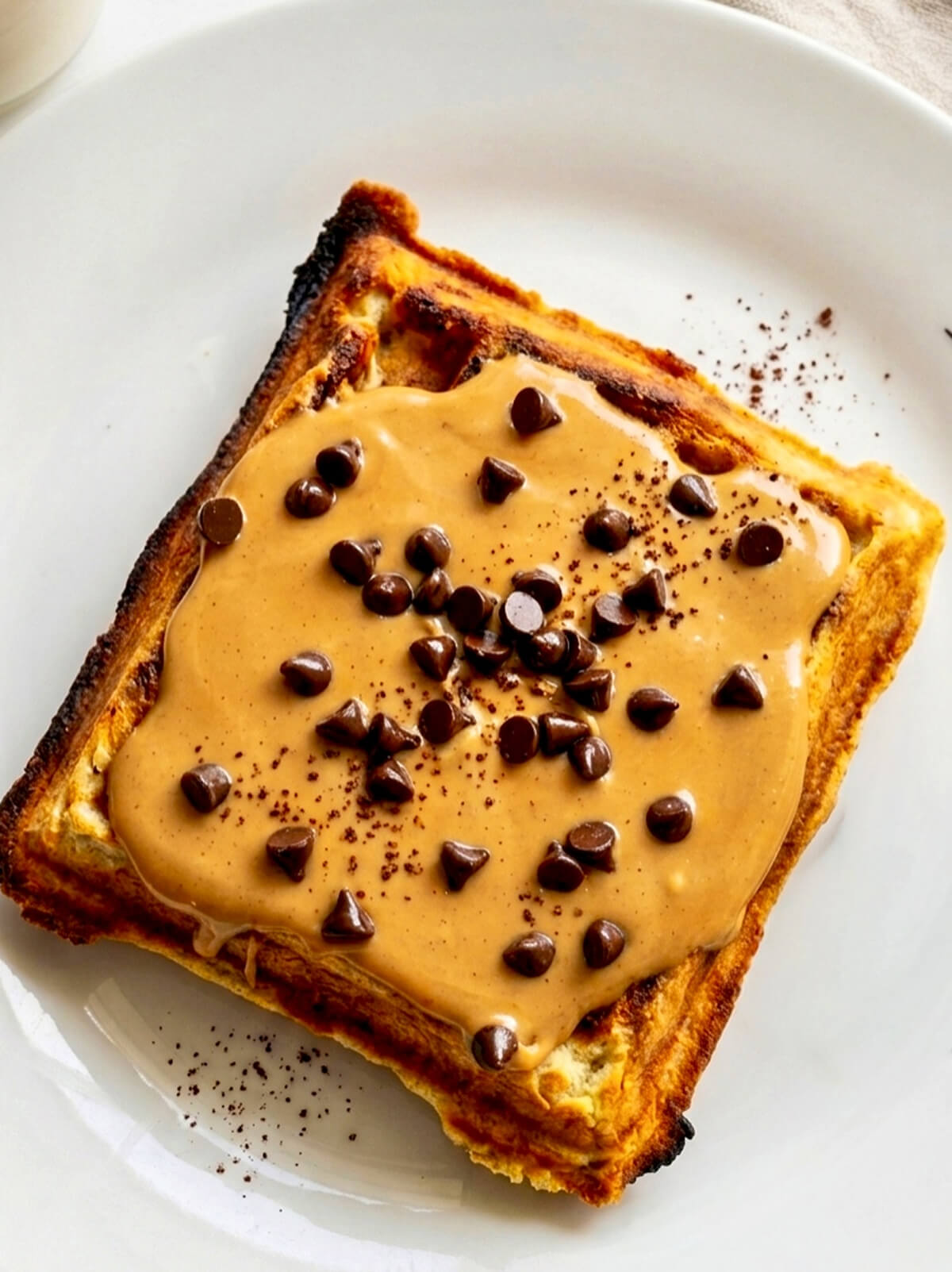 Une gaufre avec du beurre de cacahuètes et des pépites de chocolat, dans une assiette blanche.
