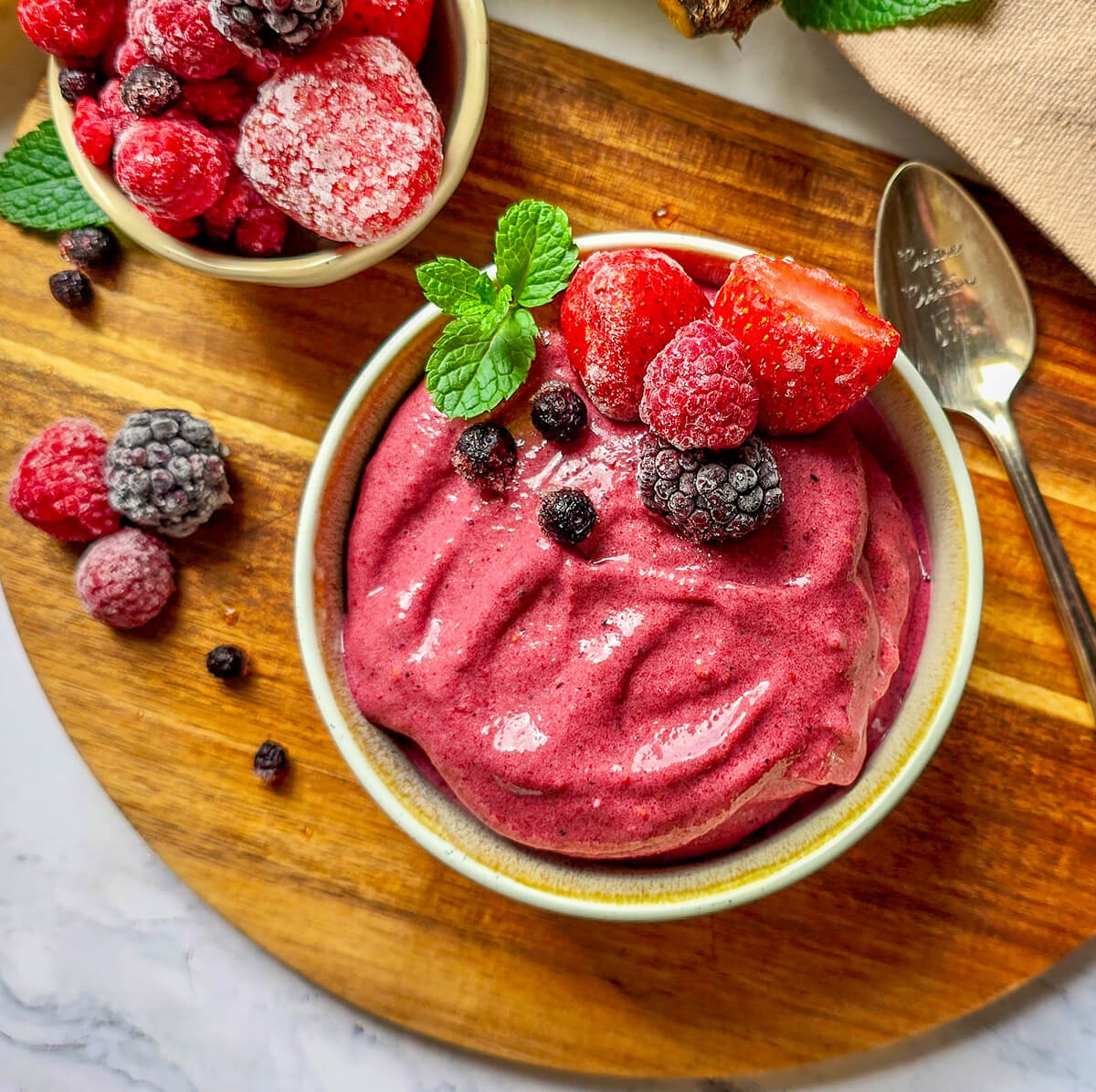 Un bol rempli de glace fruits rouges, avec des fruits surgelés sur le dessus, sur une planche de bois.
