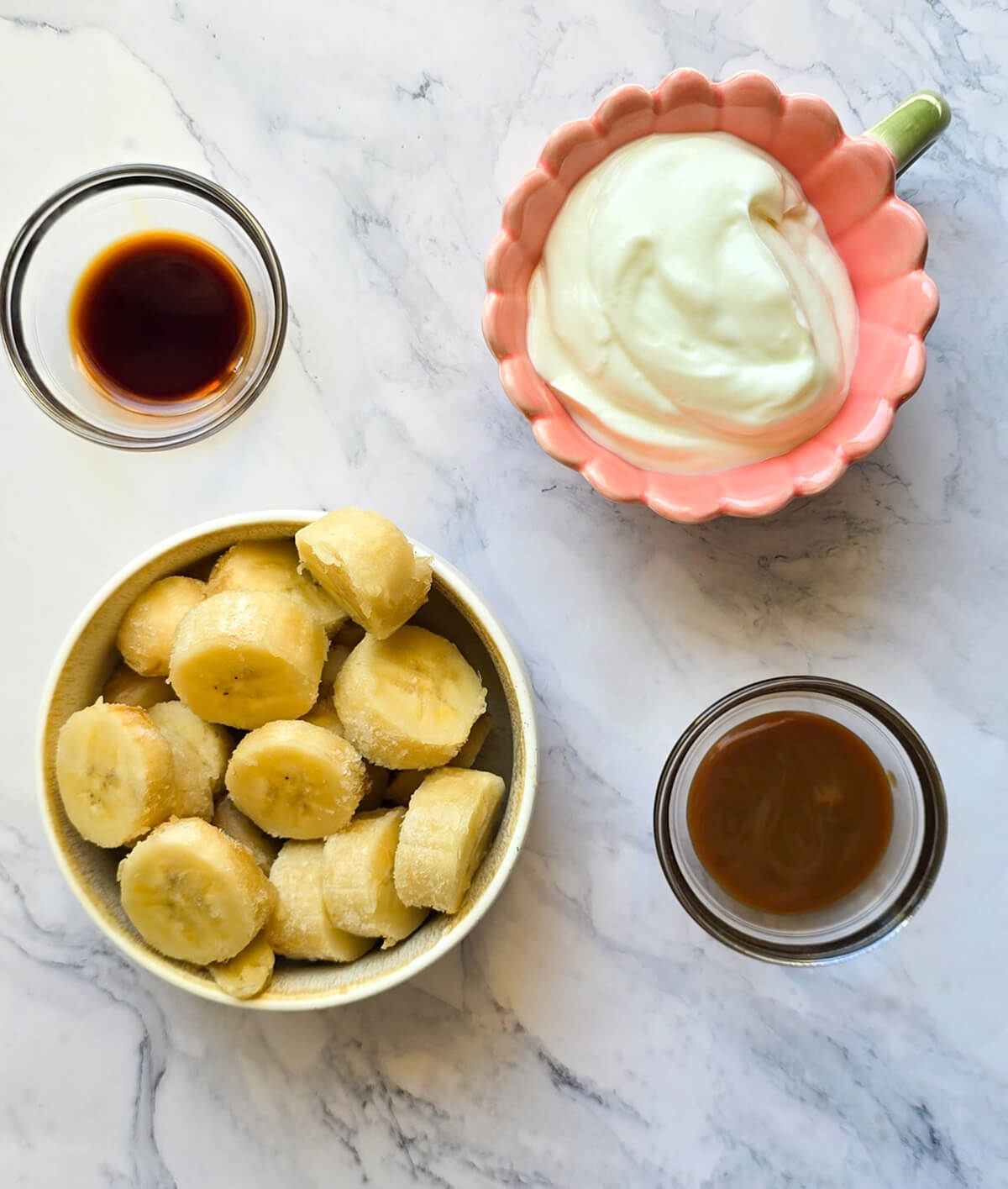 Des ingrédients pour faire un milkshake banane vanille et caramel, sur un fond blanc marbré.