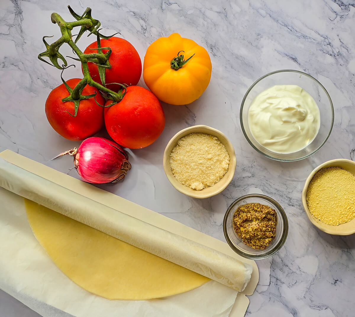 Des ingrédients pour préparer une tarte tomate moutarde sur un fond blanc marbré.