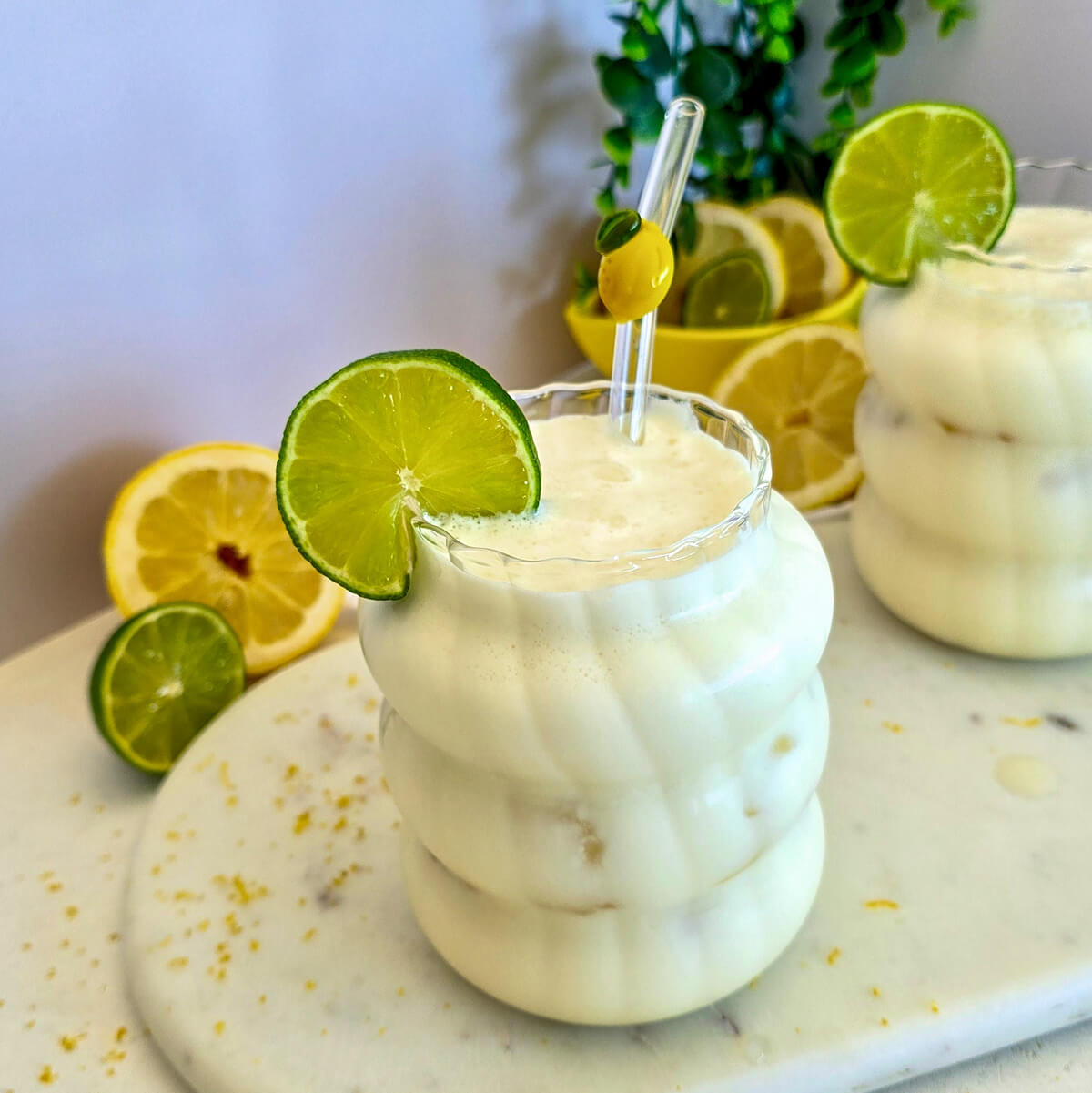 Gros plan d'une limonade brésilienne au citron vert dans un verre givré ondulé, surmonté d'une tranche de citron vert et d'une paille avec un motif de citron jaune.