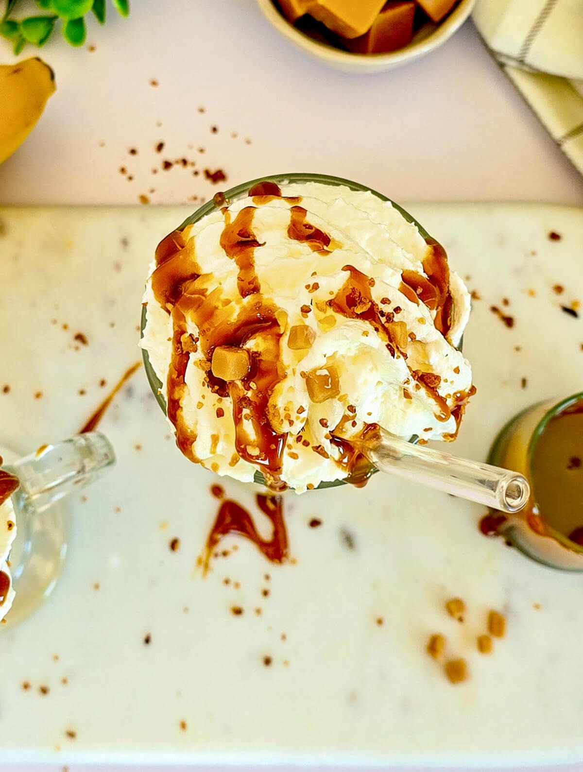 Vue de haut d'un milkshake avec de la crème chantilly et un filet généreux de caramel, avec une paille.