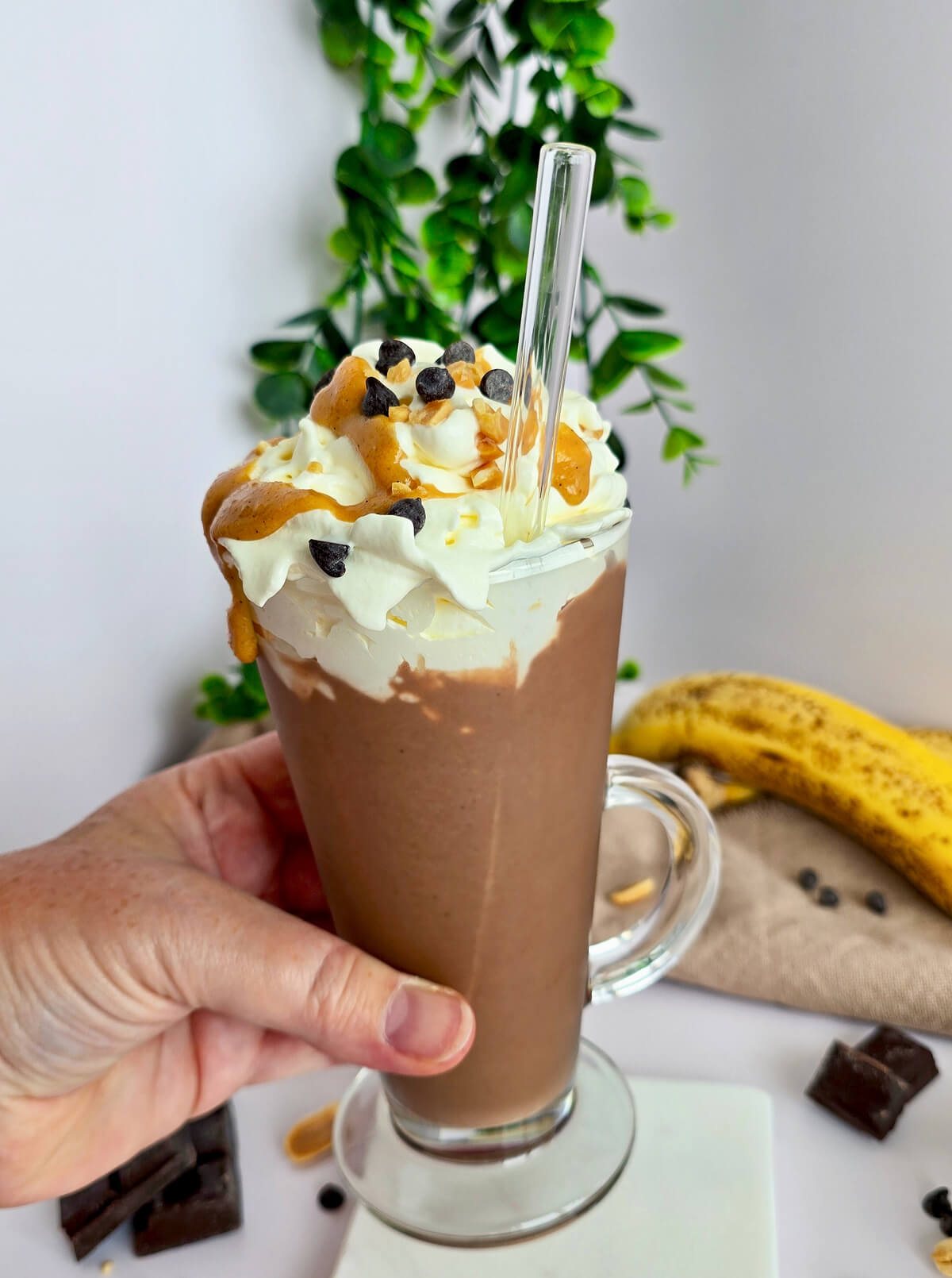 Main tenant un grand verre de milkshake Snickers crémeux sans glace, garni de chantilly et d'arachides concassées.