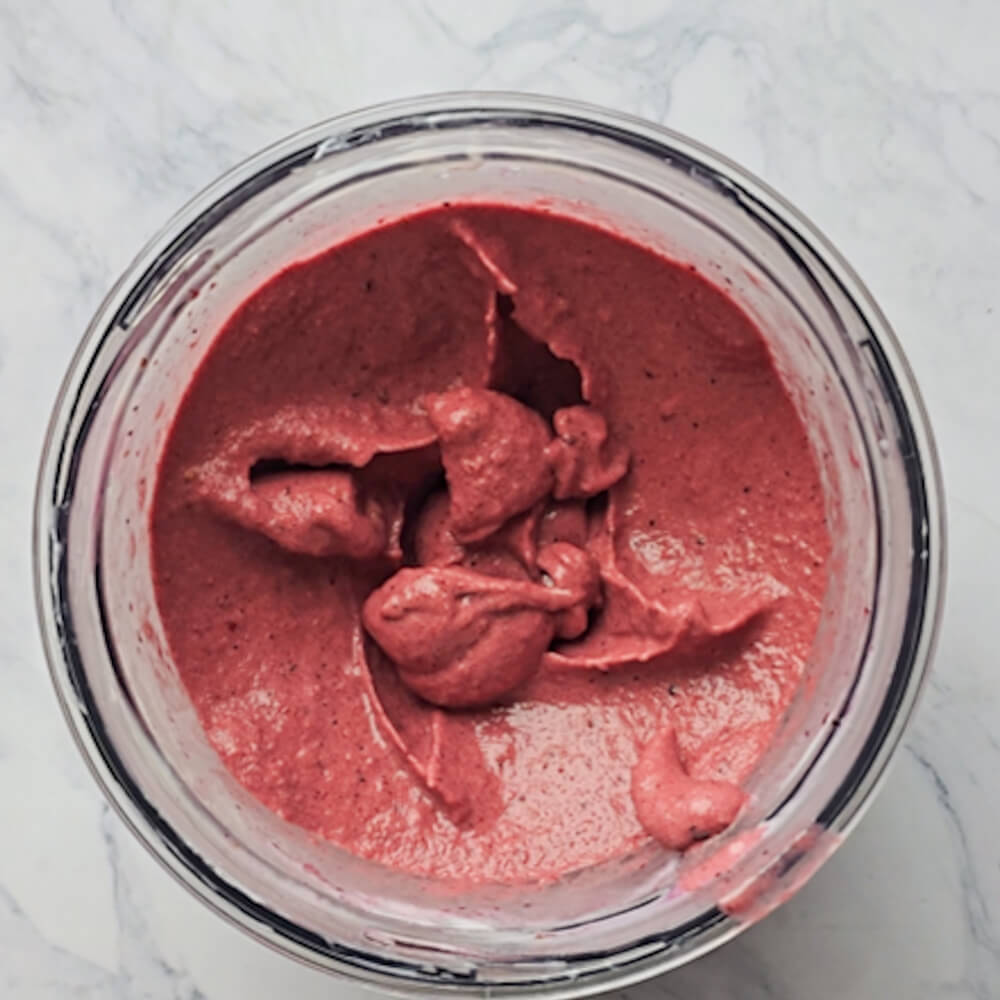 Un sorbet glace fruits rouges dans le bol d'un mini-mixeur, sur fond blanc marbré.