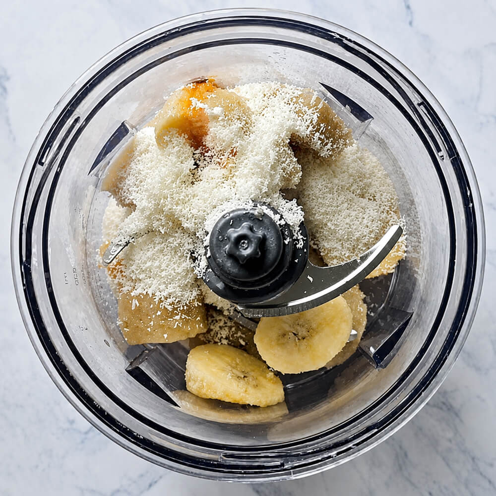 Des ingrédients pour faire une glace maison dans le bol d'un petit mixeur, sur un fond blanc marbré.