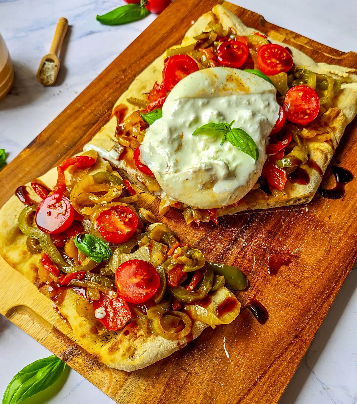 Pinsa coupée en deux, garnie de poivrons, tomates cerises et burrata crémeuse, disposée sur une planche en bois.