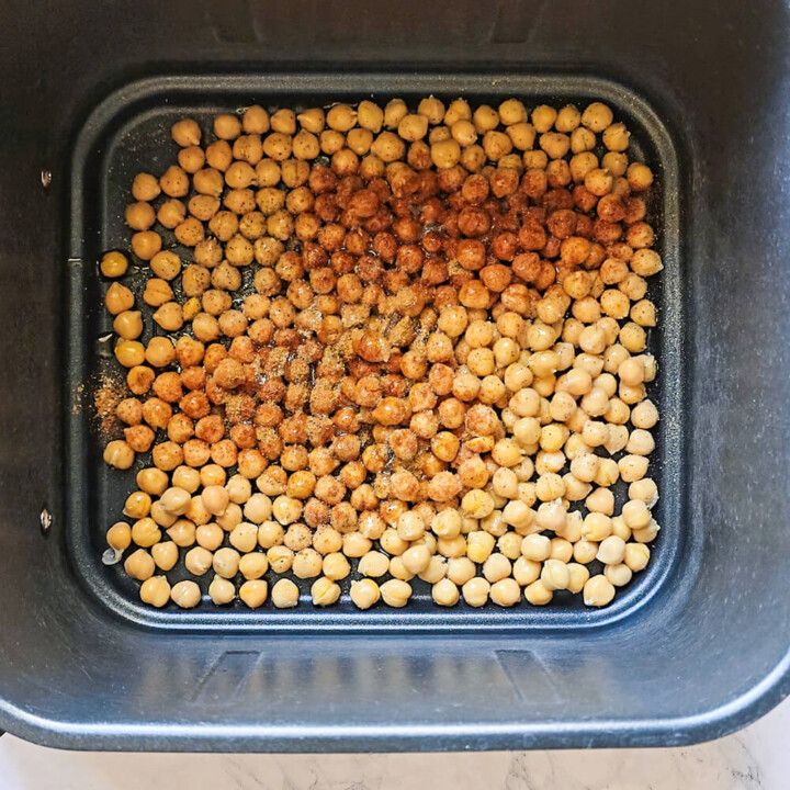 Pois chiches assaisonnés d'épices étalés uniformément dans le panier d'un airfryer avant la cuisson.