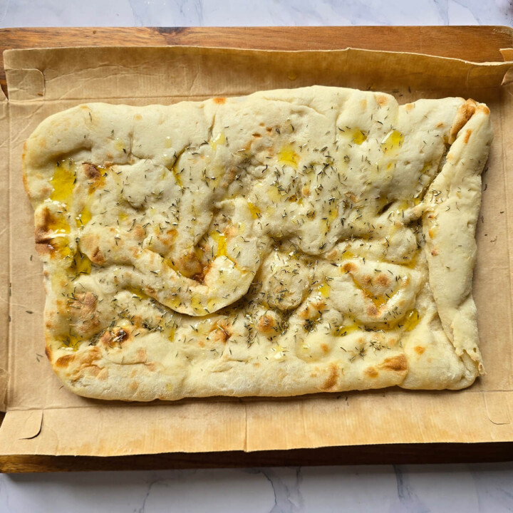 Base de pinsa précuite, assaisonnée d'herbes aromatiques et d'huile d'olive, disposée sur du papier cuisson avant d'être garnie.