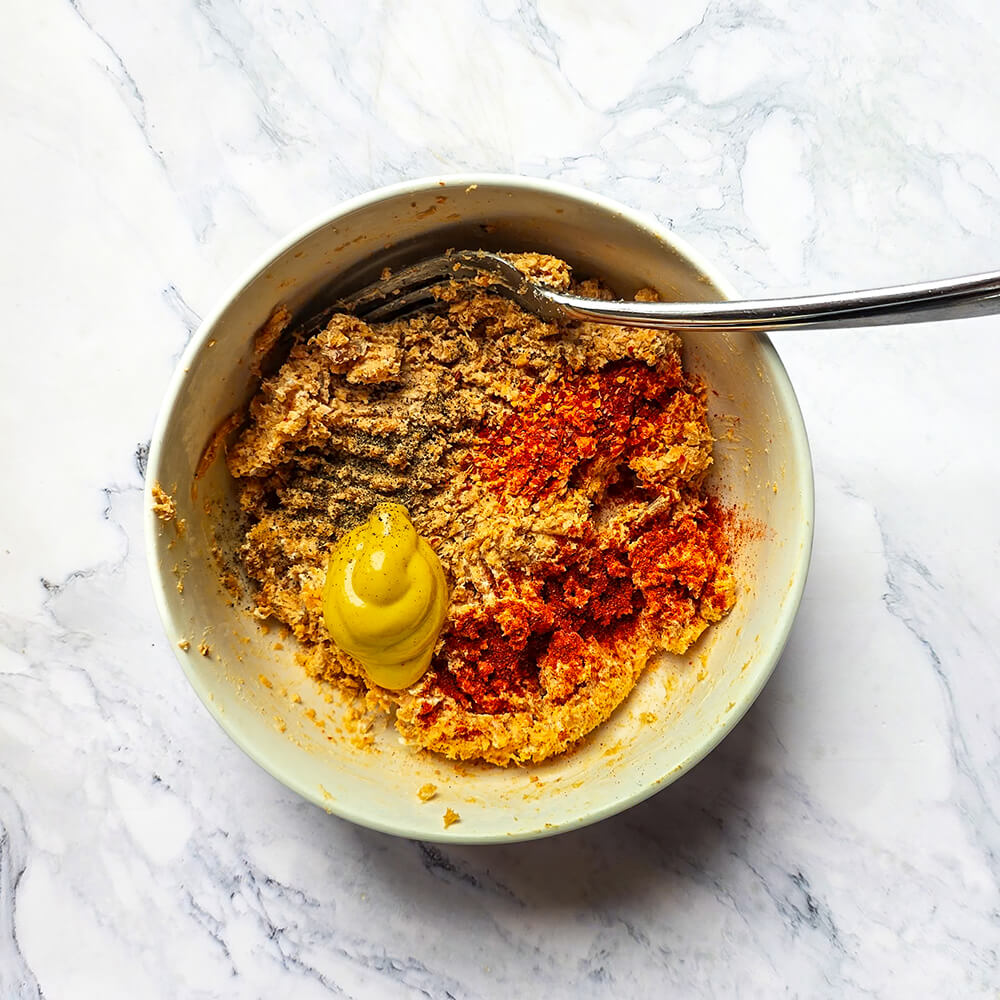 Un bol blanc contenant du poulet roti mixé avec des épices, moutarde et fromage frais.