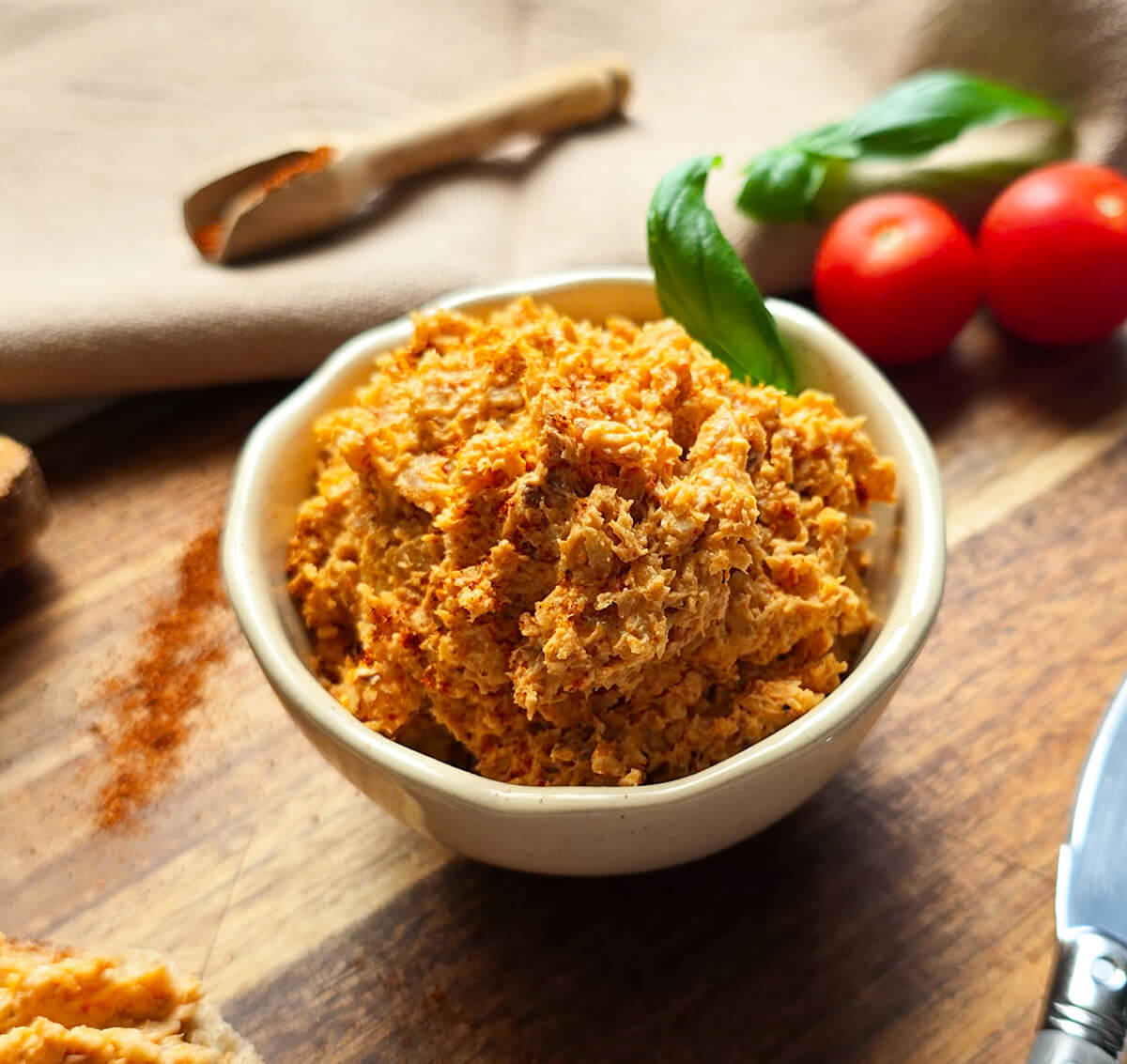 Des rillettes de poulet dans un bol blanc, sur une planche de bois, tomates cerises en arrière plan.
