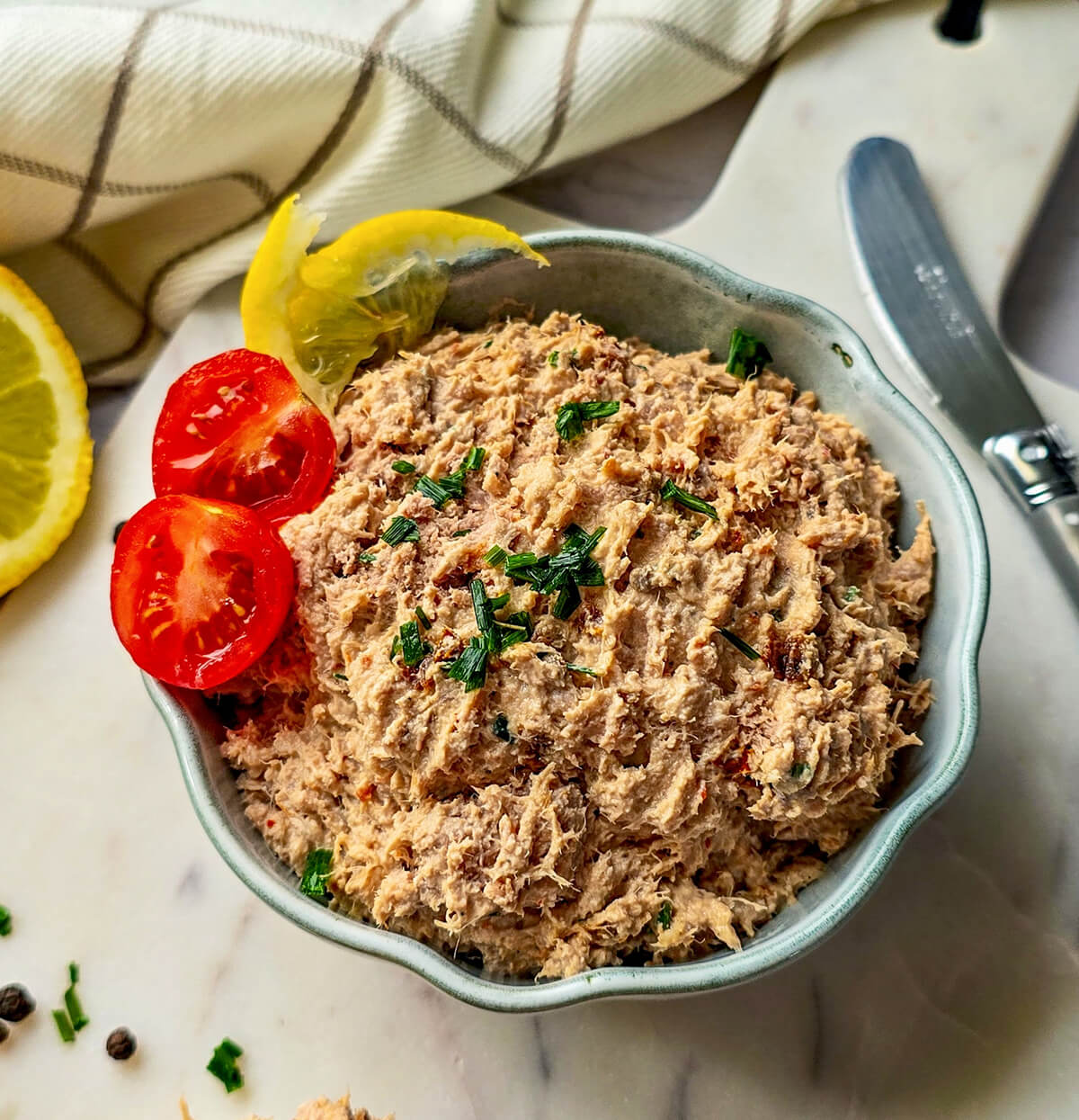 Un grand bol blanc contenant des rillettes de thon faites maison, sur un fond blanc, couteau à beurre sur le côté.