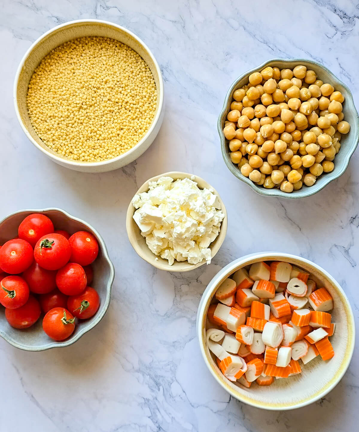 Des ingrédients sur un fond marbré blanc pour préparer une salade de perles de blé.