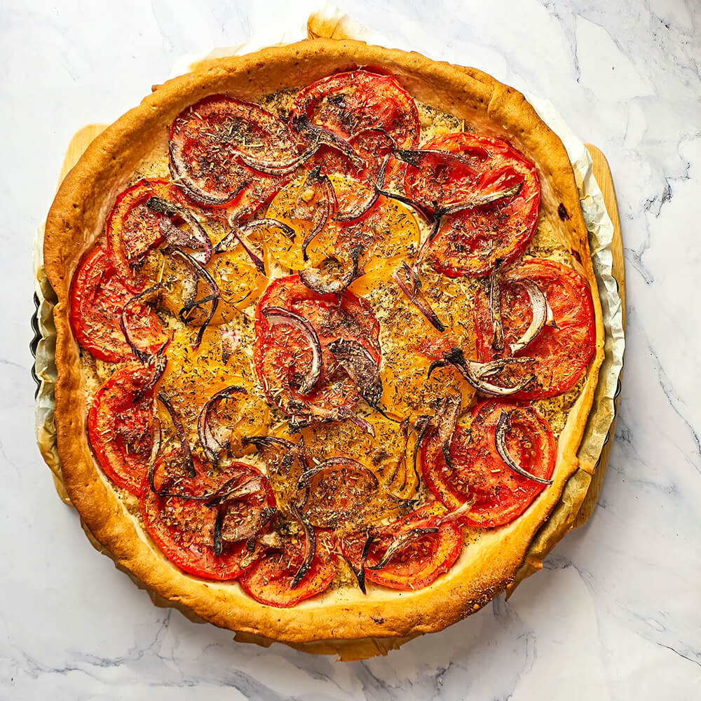 Une tarte tomate après cuisson dans son moule, sur une surface blanche marbré.