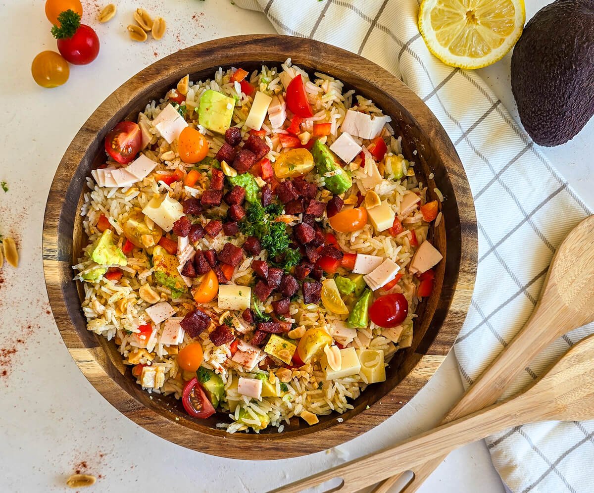 Salade Tex Mex dans un bol en bois marron, cuillère en bois, torchon blanc à carreaux et légumes sur les côtés. Le tout sur un fond blanc.