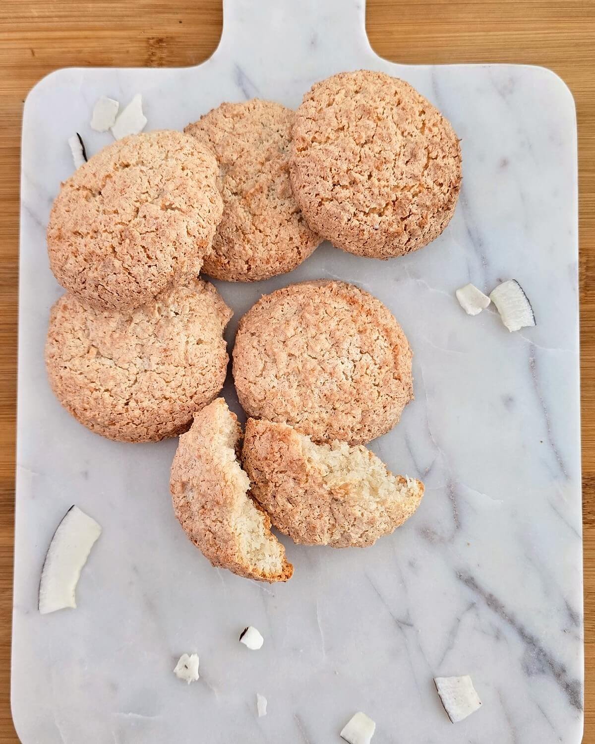 Biscuits à la noix de coco sur une planche en marbre, dont un rocher cassé en deux montrant son intérieur moelleux, entourés de copeaux de noix de coco.