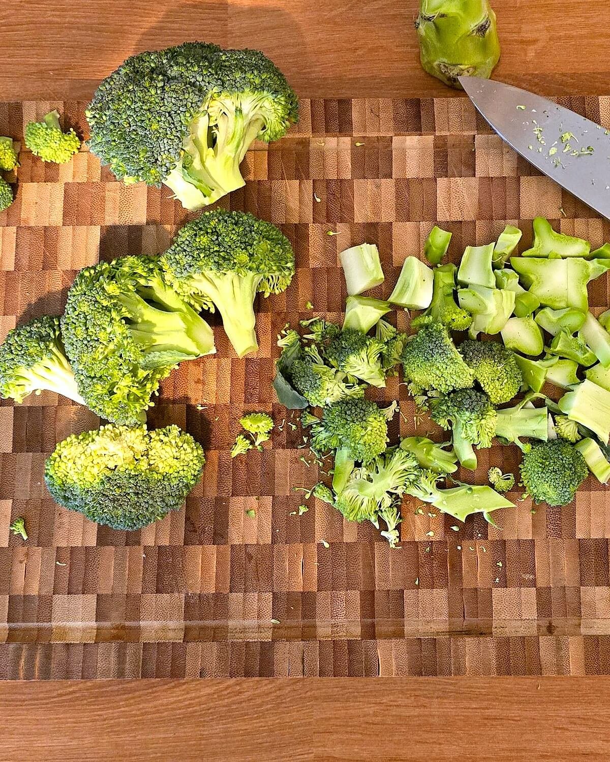 Brocoli frais découpé en fleurettes et en morceaux de tige sur une planche à découper en bois, à côté d'un couteau de chef, pour la sauce au brocoli.