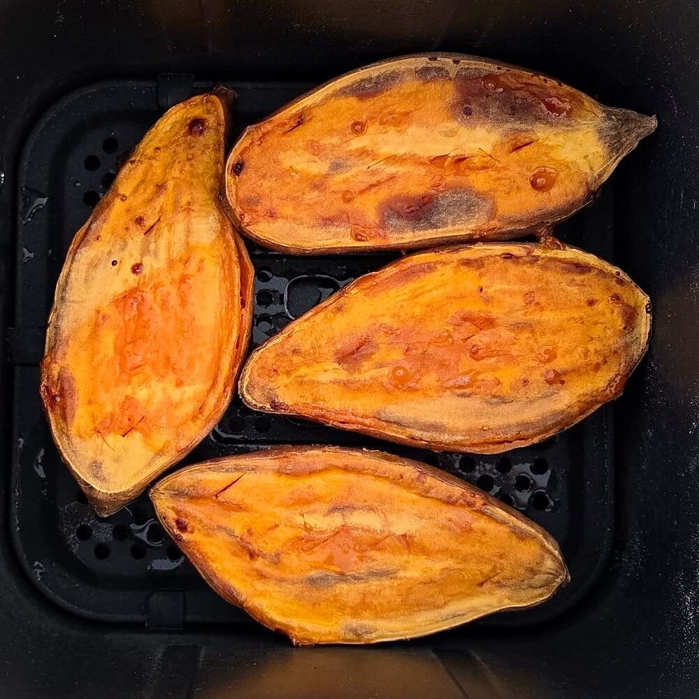 Quatre moitiés de patates douces rôties, chair dorée vers le haut, dans le panier d'un Airfryer.